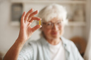 Food, nutrition, diet and health concept. Close up shot of elderly woman's hand holding fish oil or omega-3 polyunsaturated fatty acid supplement in shape of capsule, going to take one during lunch