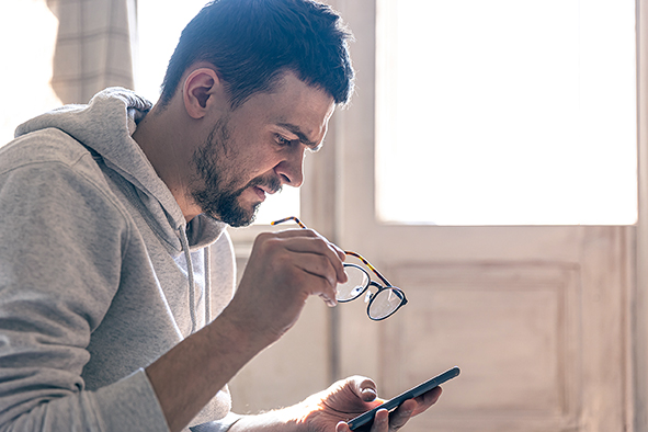 A man with glasses in his hands, uses a smartphone, blurred background, copy space.
